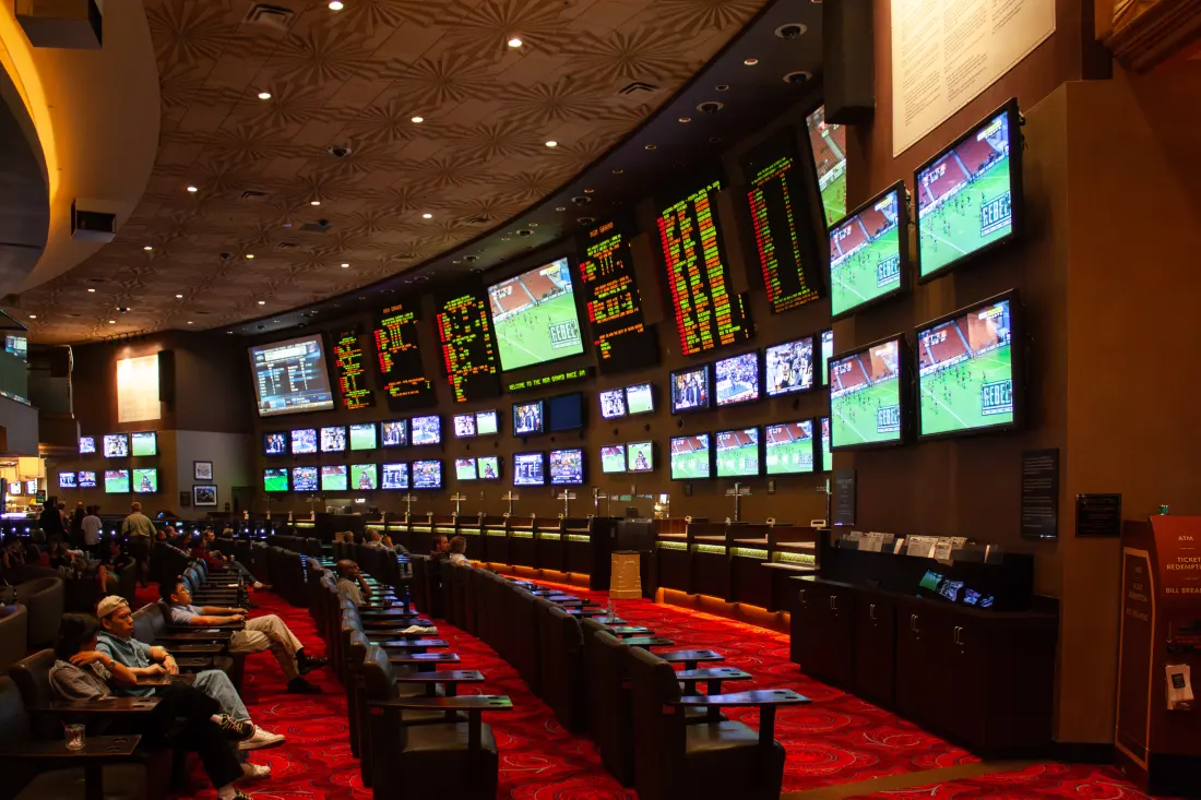 An odds board and rows of screens above the seats of a large sportsbook